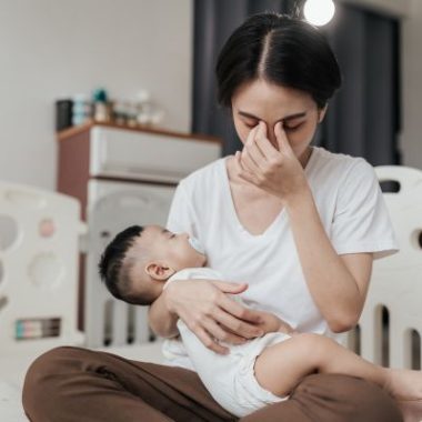 A mother holding her baby appears tired.