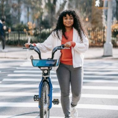 A teen girl with long dark hair walks a blue bike.