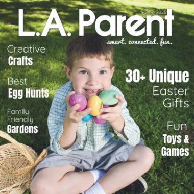 Young boy holding colorful Easter eggs while sitting on grass with basket, featured on L.A. Parent spring 2026 cover