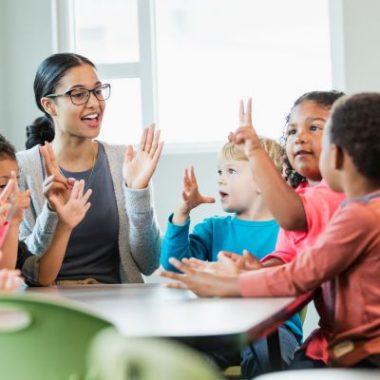 Teacher guides elementary students as they complete classroom assignments using paper and pencils.