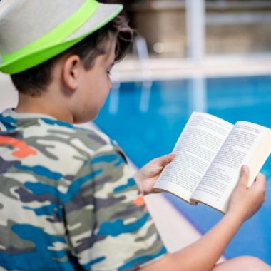A child reads a book alongside a pool. Reading is fundamental in preventing summer learning loss.