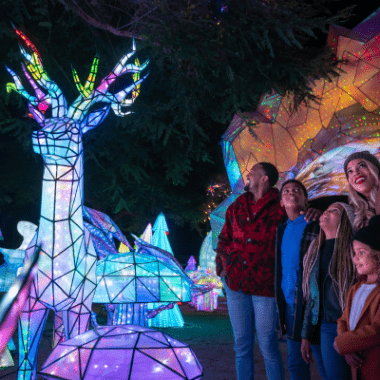 A family looks up at a lit holiday sculpture.